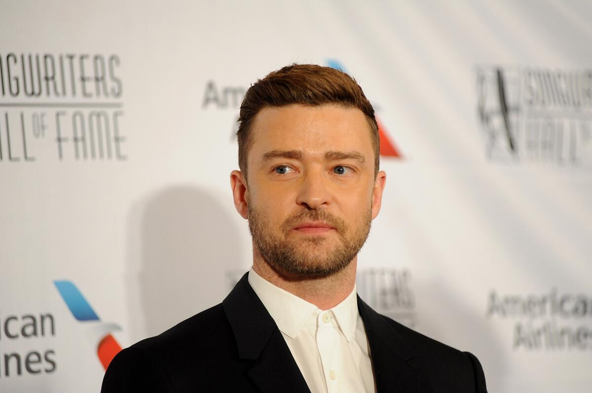 Justin Timberlake in a black suit looking to the side while standing in front of a white backdrop
