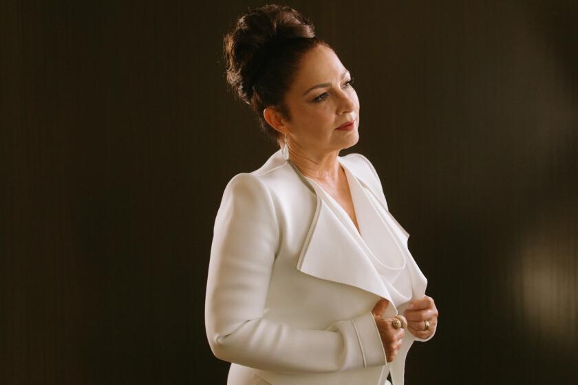 Side profile of Gloria Estefan holding the front of a white jacket against a metal background