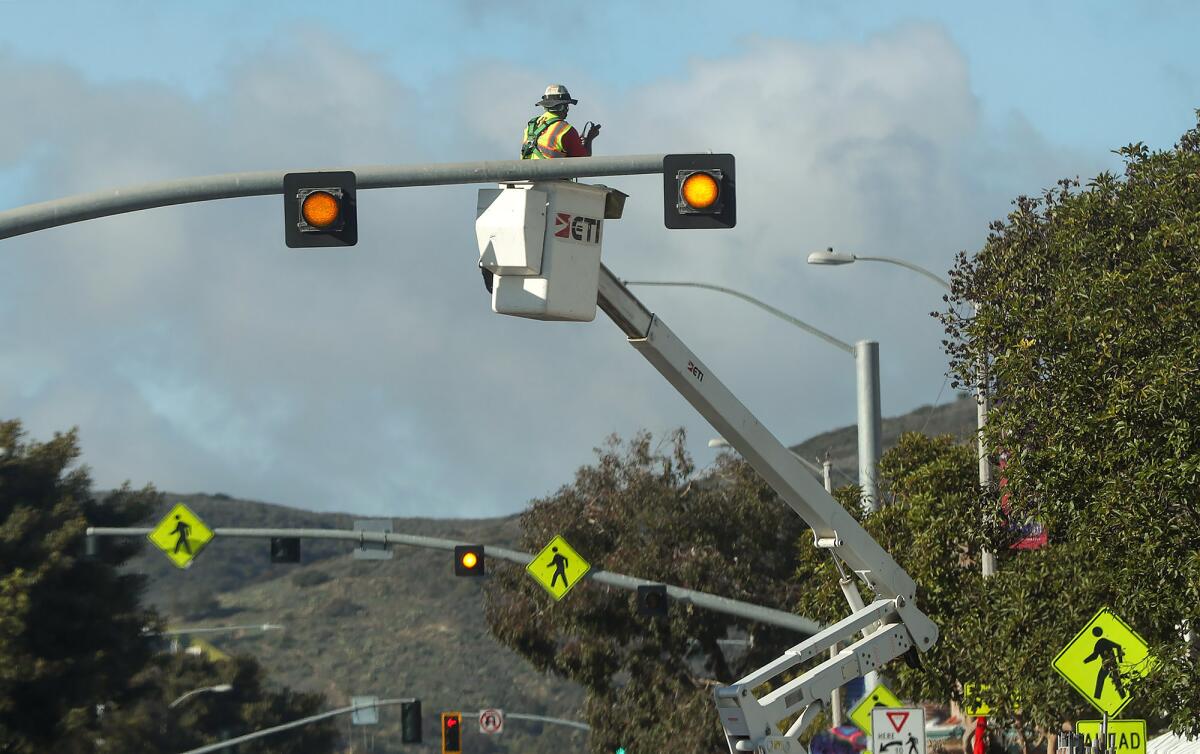 A Caltrans worker installs flashing overhead lights above the crosswalk to enhance pedestrian safety in Laguna Beach.