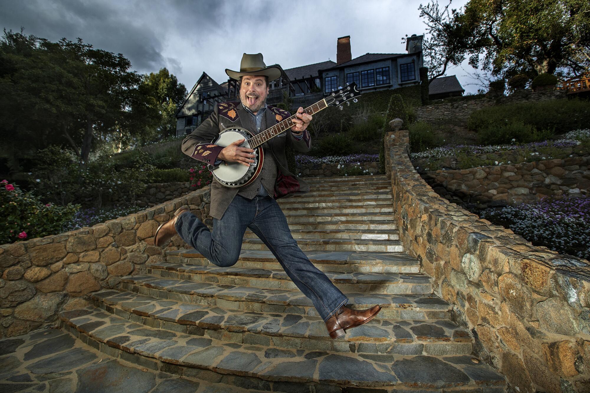 Jared Gutstadt, holding a banjo, leaps across the stairs at his Mandeville Canyon compound