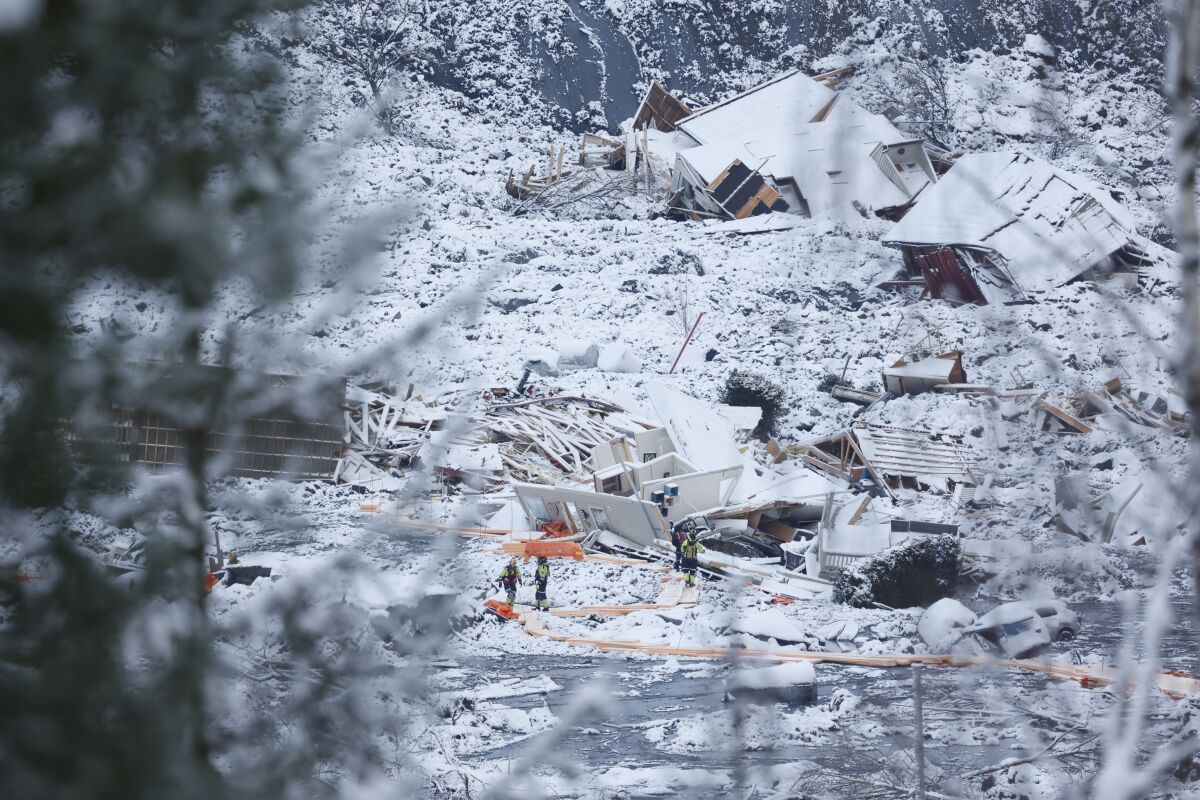 Rescue crews work in snowy terrain amid wrecked buildings and debris.