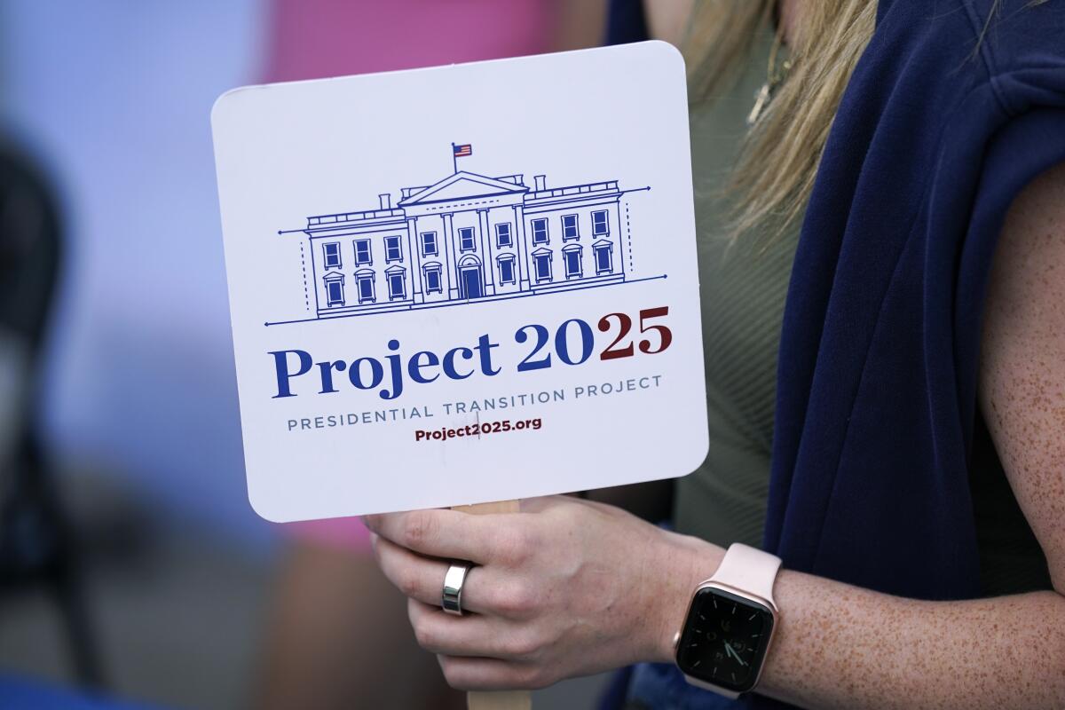 A woman holds a fan bearing an image of the White House and the words 'Project 2025'