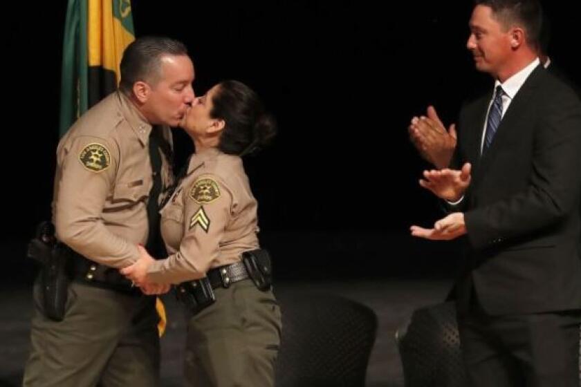 MONTEREY PARK, CA-DECEMBER 3, 2018: Alex Villanueva, left, the new Los Angeles County Sheriff, kisses his wife Vivian after being sworn in during a ceremony at East Los Angeles College in Monterey Park on December 3, 2018. 2nd from right is his son Jared Villanueva, an army veteran who served in Iraq, and at right is his granddaughter Christy Villanueva. (Mel Melcon/Los Angeles Times)