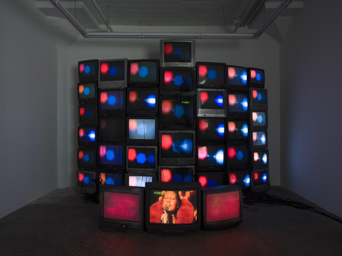A stack of old TVs are arranged in the form of a curving wall, with three monitors at the base showing Aretha Franklin.