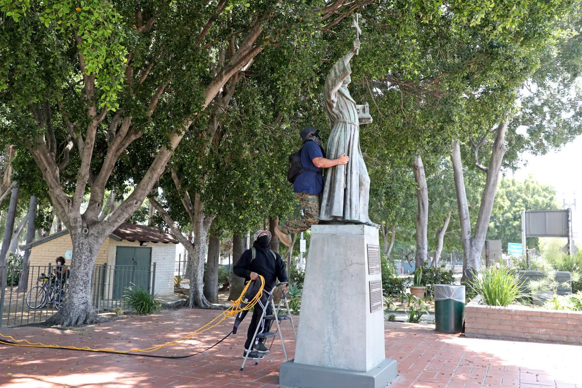 Two men secure ropes to a statue of Junipero Serra as they prepare to topple it