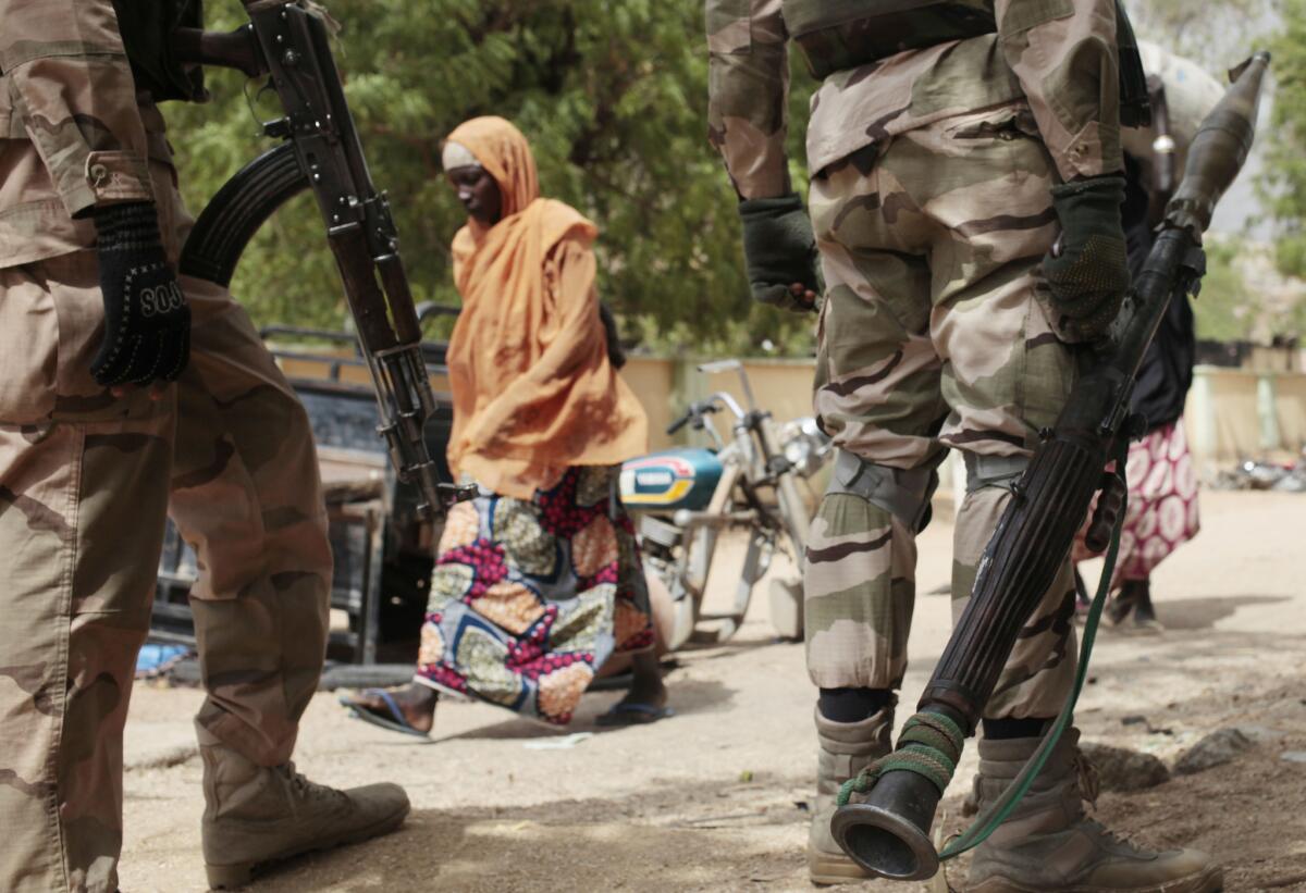 A woman walks past Nigerian soldiers at a checkpoint in Gwoza, Nigeria, a town newly liberated from Boko Haram, in April 2015.