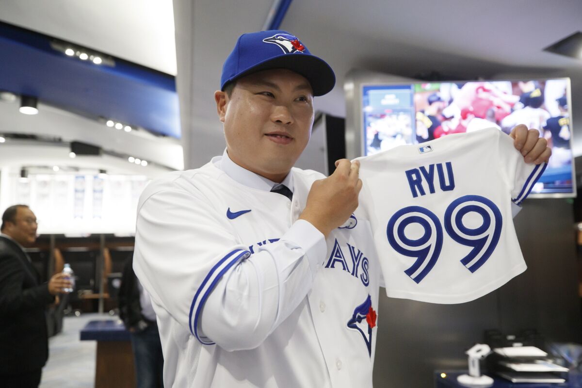 FILE - In this Friday, Dec. 27, 2019 file photo,Toronto Blue Jays newly signed pitcher Hyun-Jin Ryu holds up a jersey for his expected baby following a news conference announcing his signing to the team in Toronto. Hyun-Jin Ryu is now the clear and undisputed ace of a major league rotation — with all the pressure and responsibility that comes with that. What the Blue Jays need is some stability in their rotation. They used 21 different starters last year, then made several additions in the offseason. Ryu was the most prominent acquisition. (Cole Burston/The Canadian Press via AP, File)