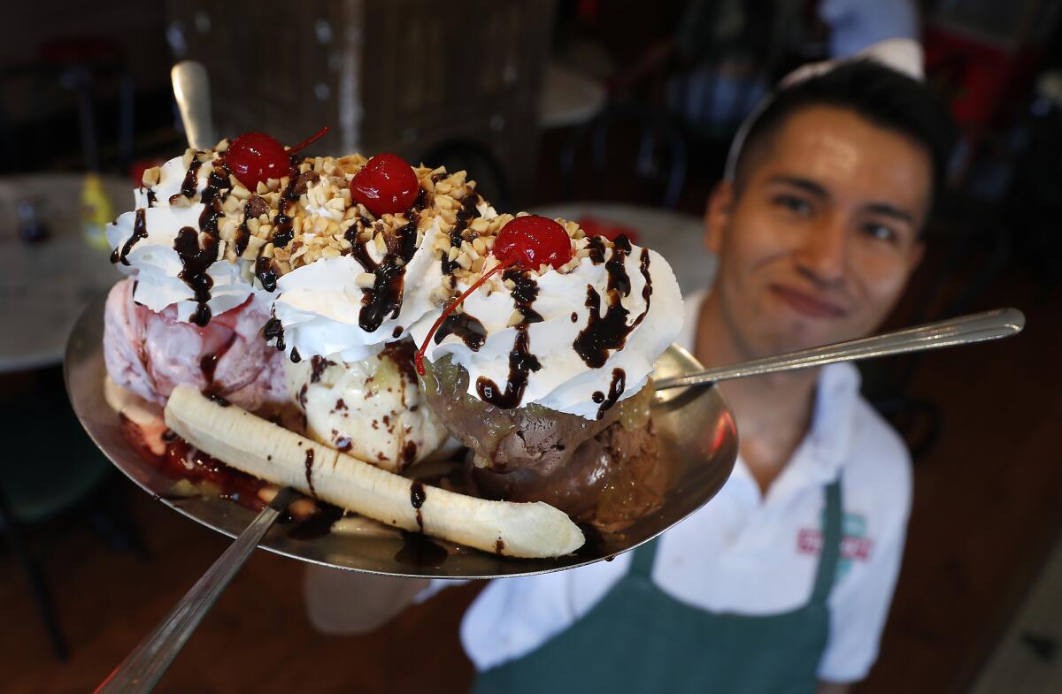 Employee Will Lopez holds up a towering banana split, the soda fountain's most popular sundae.