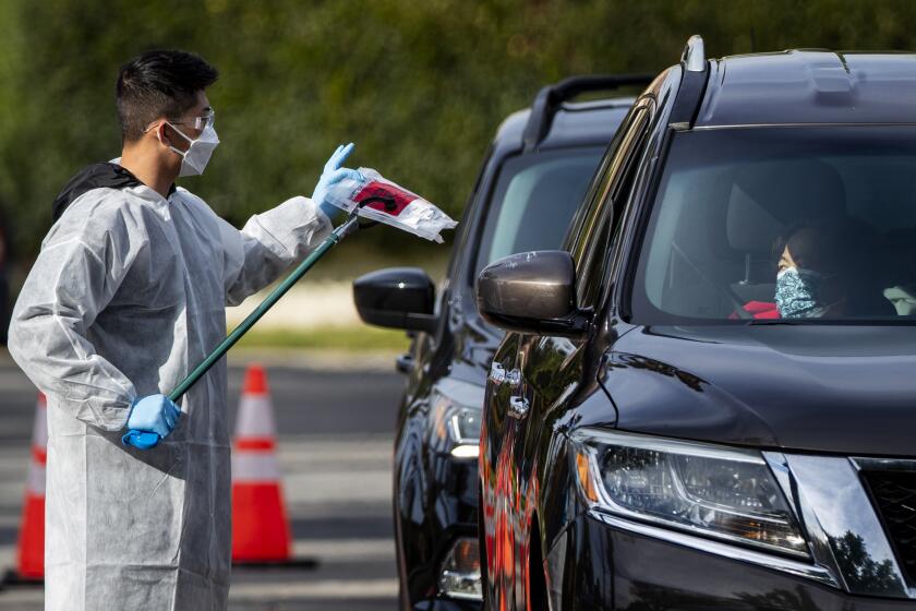 RIVERSIDE, CA - DECEMBER 21, 2021: A health care worker hands out a COVID-19 test kit at a Curative drive through testing site at La Sierra Park December 21, 2021 in Riverside, California.The Omicron variant is on the rise in Southern California and has a higher chance of infecting the unvaccinated.(Gina Ferazzi / Los Angeles Times)