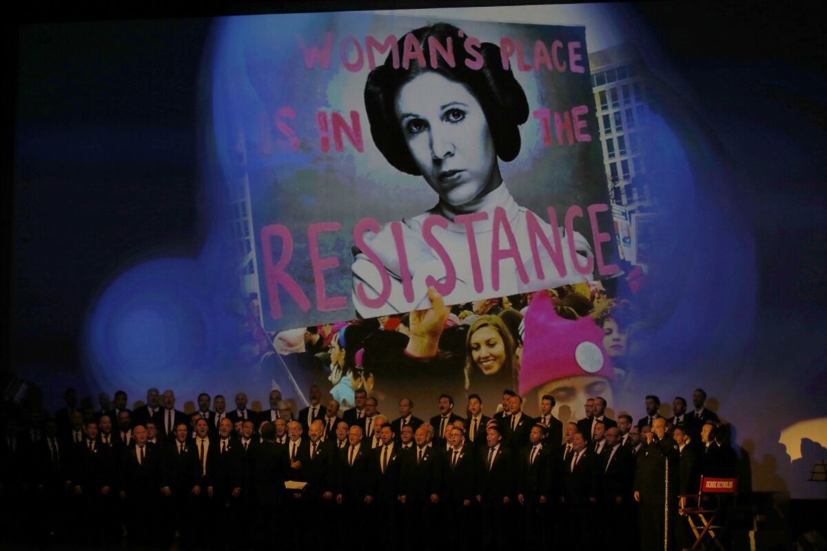 The Gay Men's Chorus of Los Angeles sings during a memorial service as images of Carrie Fisher flash on a screen in the background.