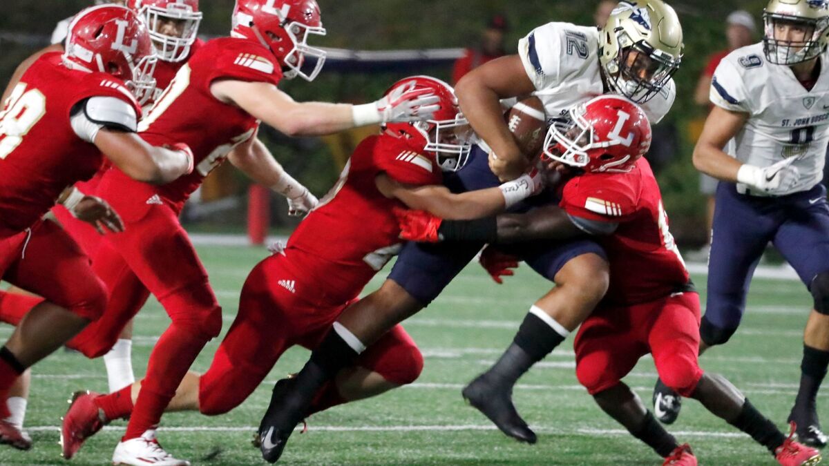 A pack of Orange Lutheran defenders try to stop St. John Bosco quarterback DJ Uiagalelei as he gains yardage during their Trinity League game last season.