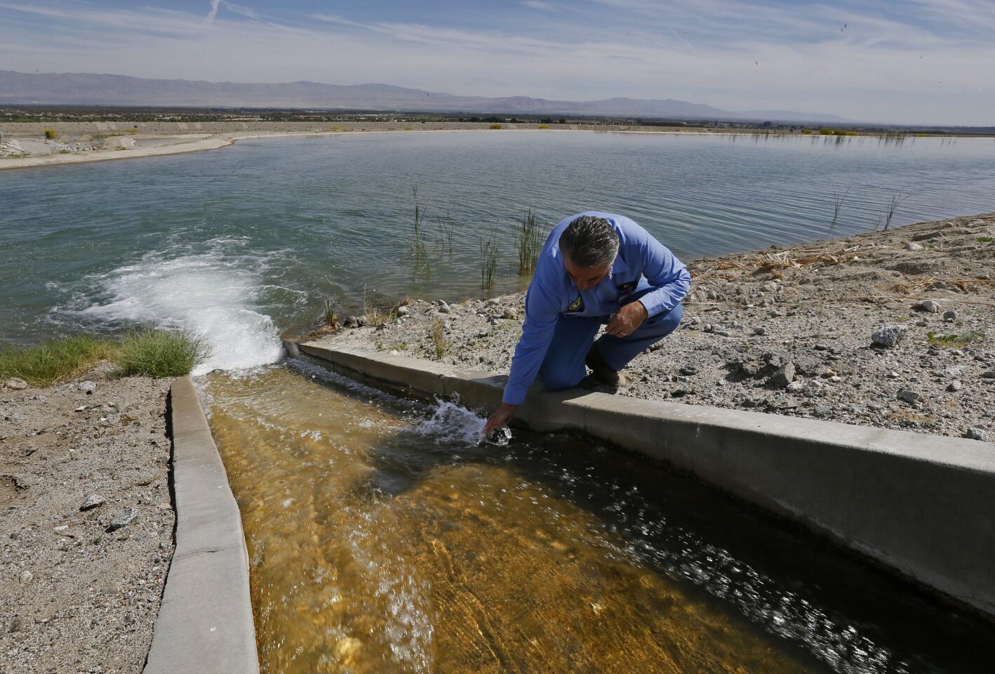 Coachella Valley Water District zanjero Ken Gray kneels at a flume at a water-replenishment basin.