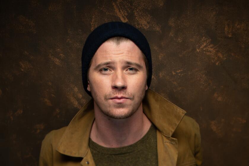 Garrett Hedlund posing in a black beanie and brown jacket