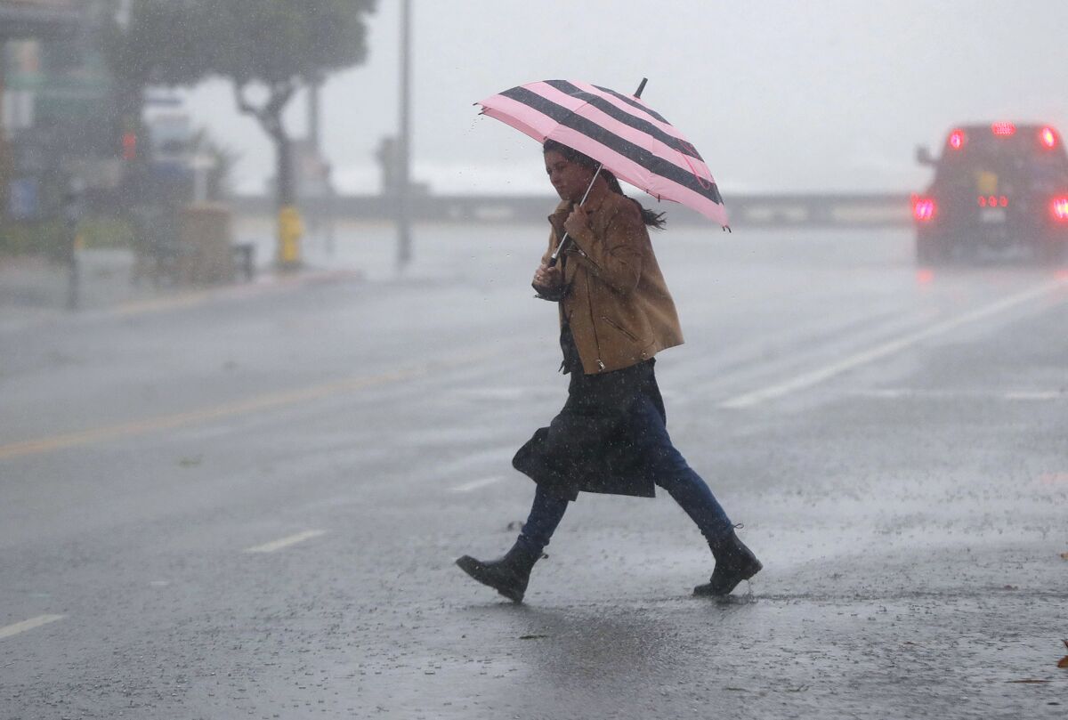 A woman braves strong wind and rain as she crosses an empty Broadway Boulevard on Tuesday morning in Laguna Beach.