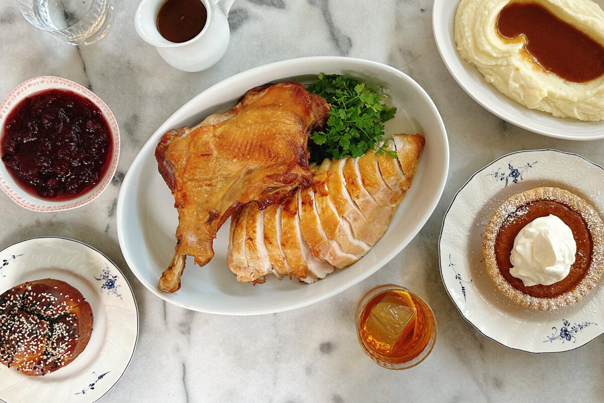 Sliced turkey in a white oval dish, surrounded by sides and desserts