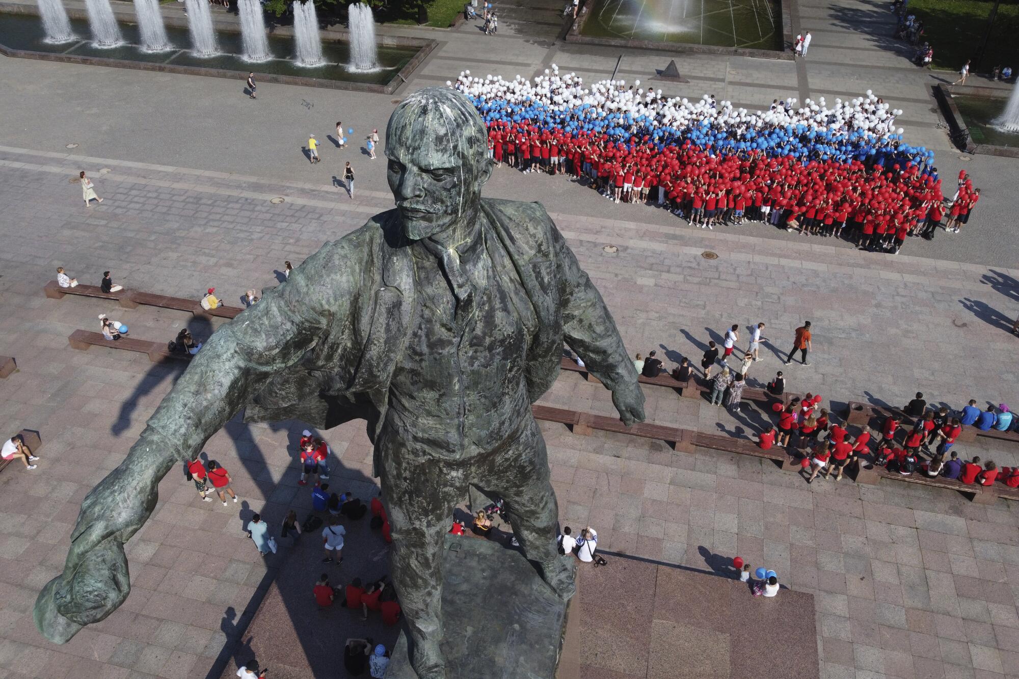 A giant statue towers over people wearing white, blue or red clothes.