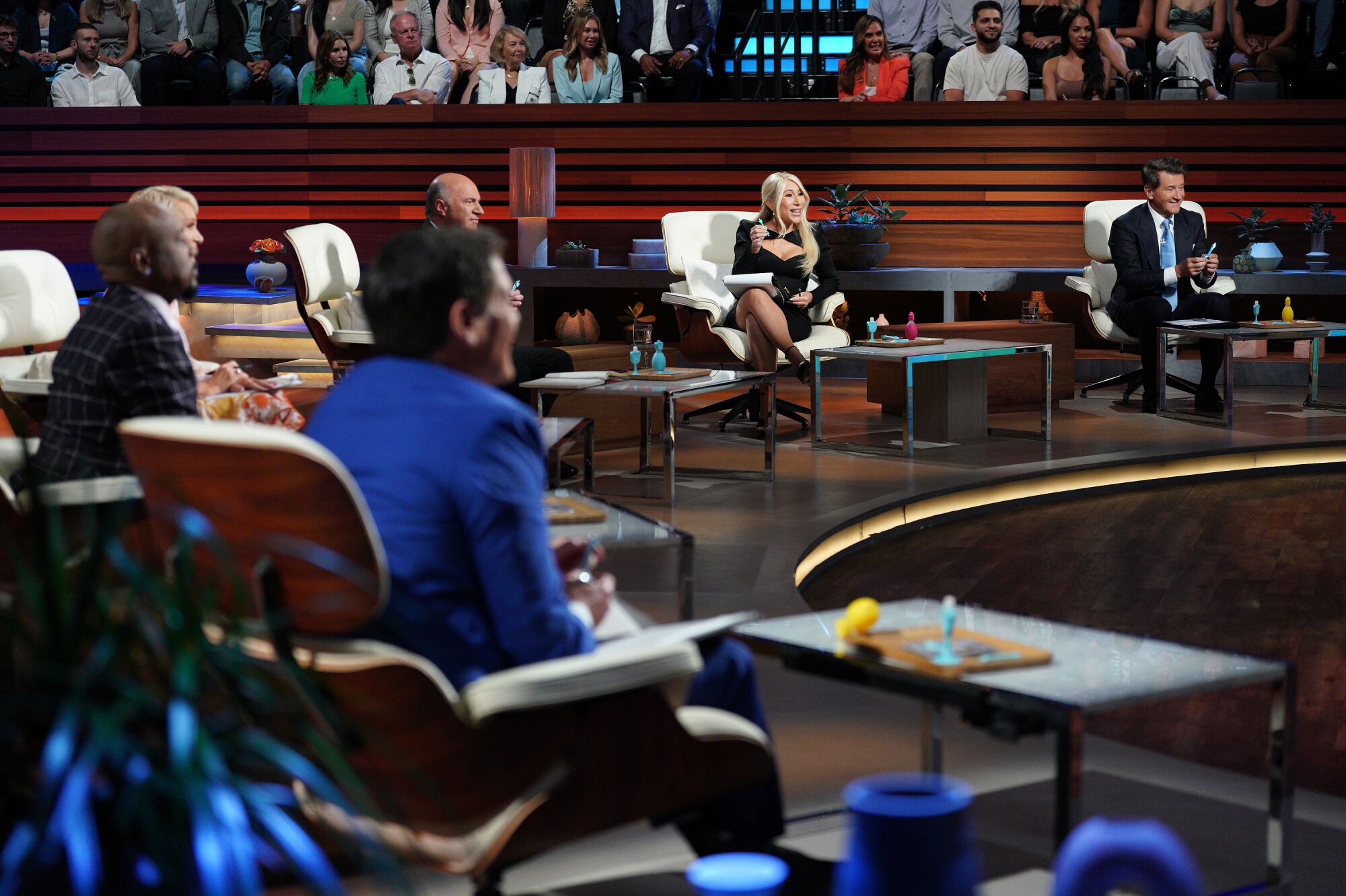 "Shark Tank" celebrity panelists sit at a curved dais during taping as a studio audience looks on