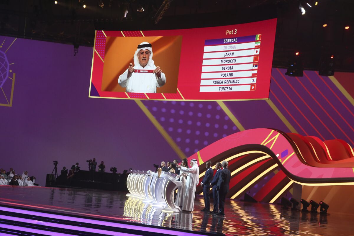 Former Qatari soccer international Adel Ahmed MalAllah holds up the name of Senegal the 2022 soccer World Cup draw at the Doha Exhibition and Convention Center in Doha, Qatar, Friday, April 1, 2022. (AP Photo/Hussein Sayed)