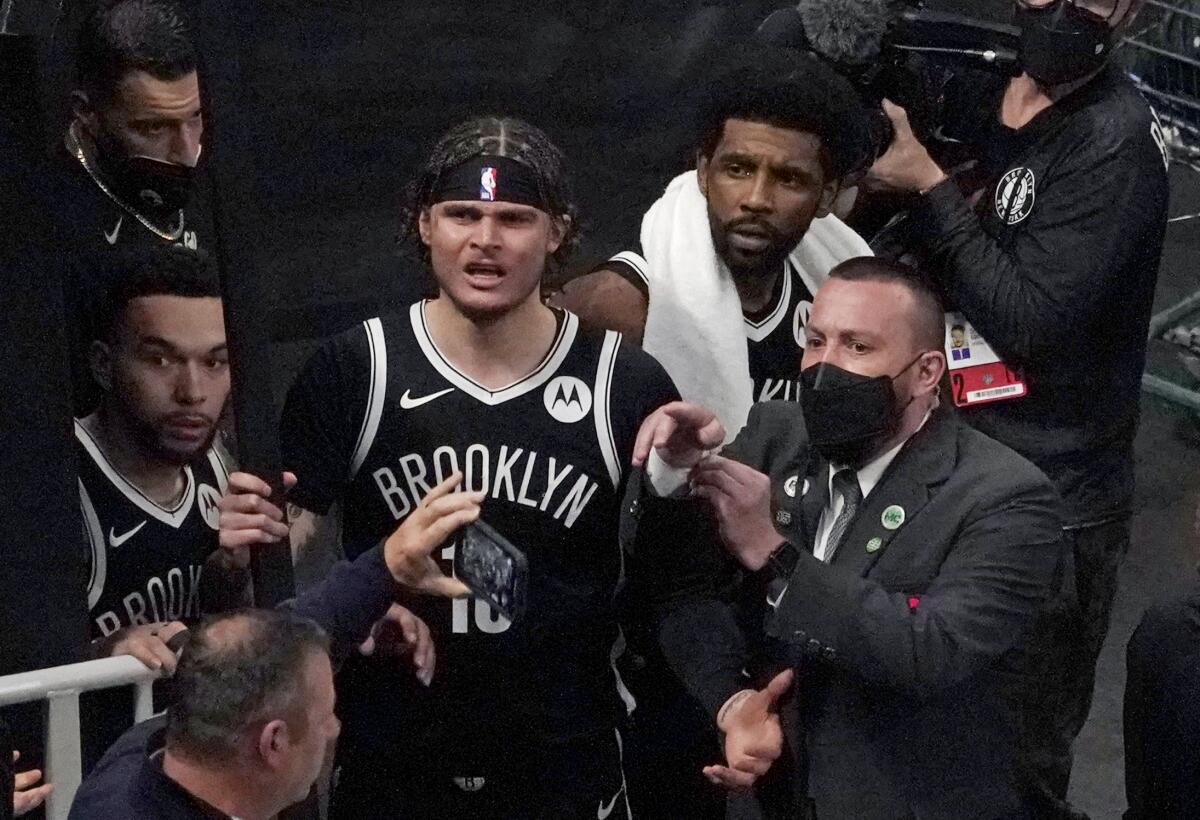 A security guard points as Brooklyn Nets' Kyrie Irving and Tyler Johnson look into the stands.