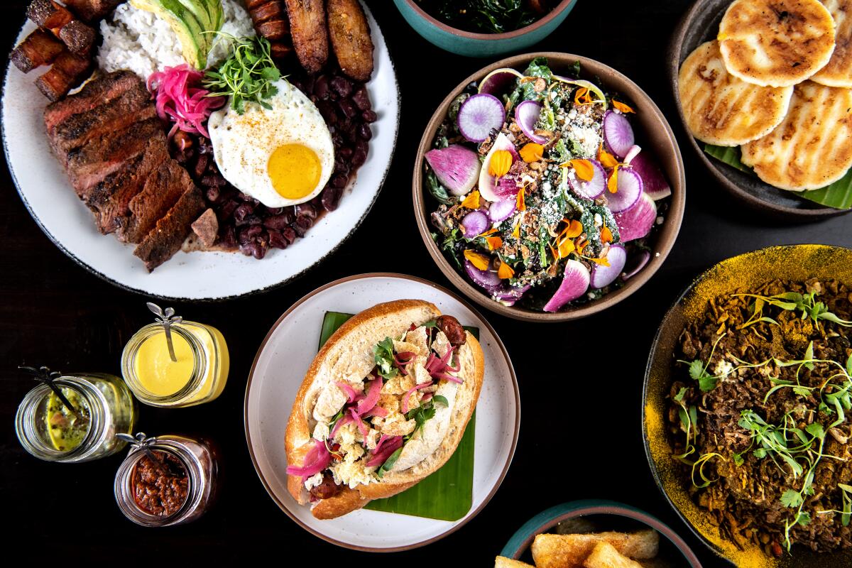 LONG BEACH, CA - JUNE 10: An array oof dishes from Selva, clockwise from top left: Bandeja paisa, market braised greens, corn arepa, arroz chaufa, yucca fries, Colombian hot dog, and market green salad on Friday, June 10, 2022 in Long Beach, CA. (Mariah Tauger / Los Angeles Times)