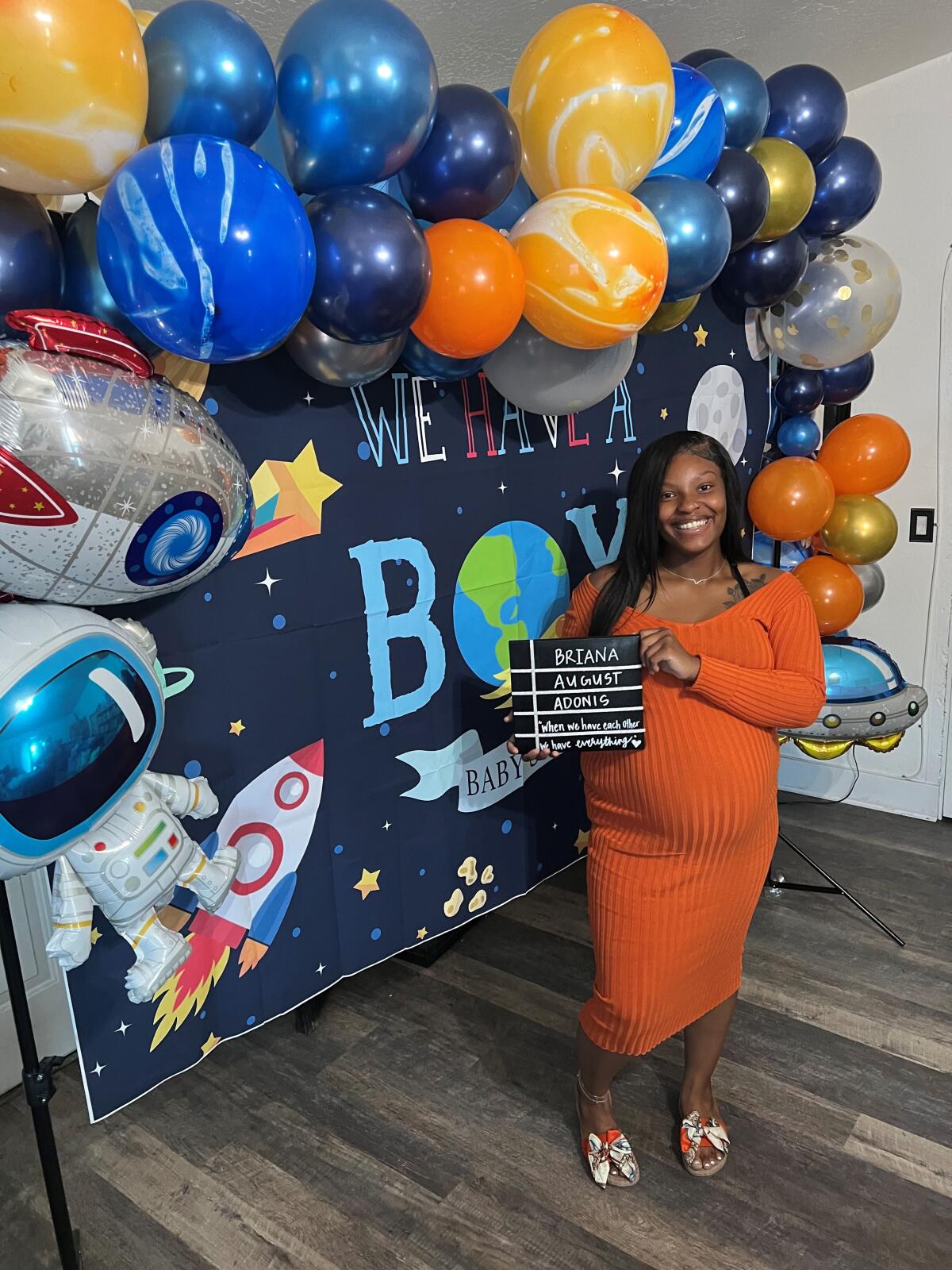 A pregnant woman stands with balloons.