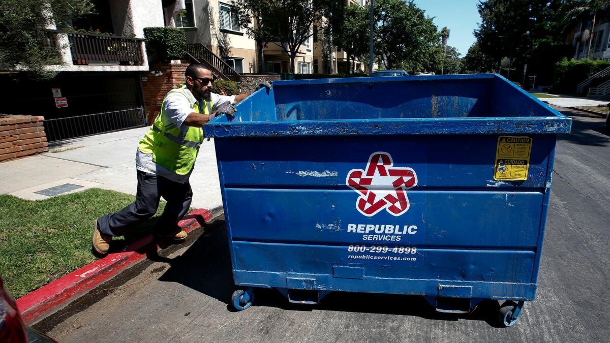 An employee with the trash company Athens Services moves a Republic Services trash bin into position for pickup in West Los Angeles. Reports of missed collections have steadily grown over the past six months under the city's RecycLA program.