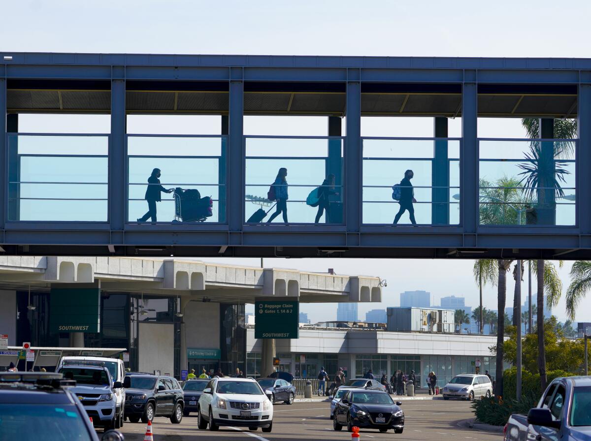 Travelers with luggage cross a bridge over traffic at San Diego International Airport 