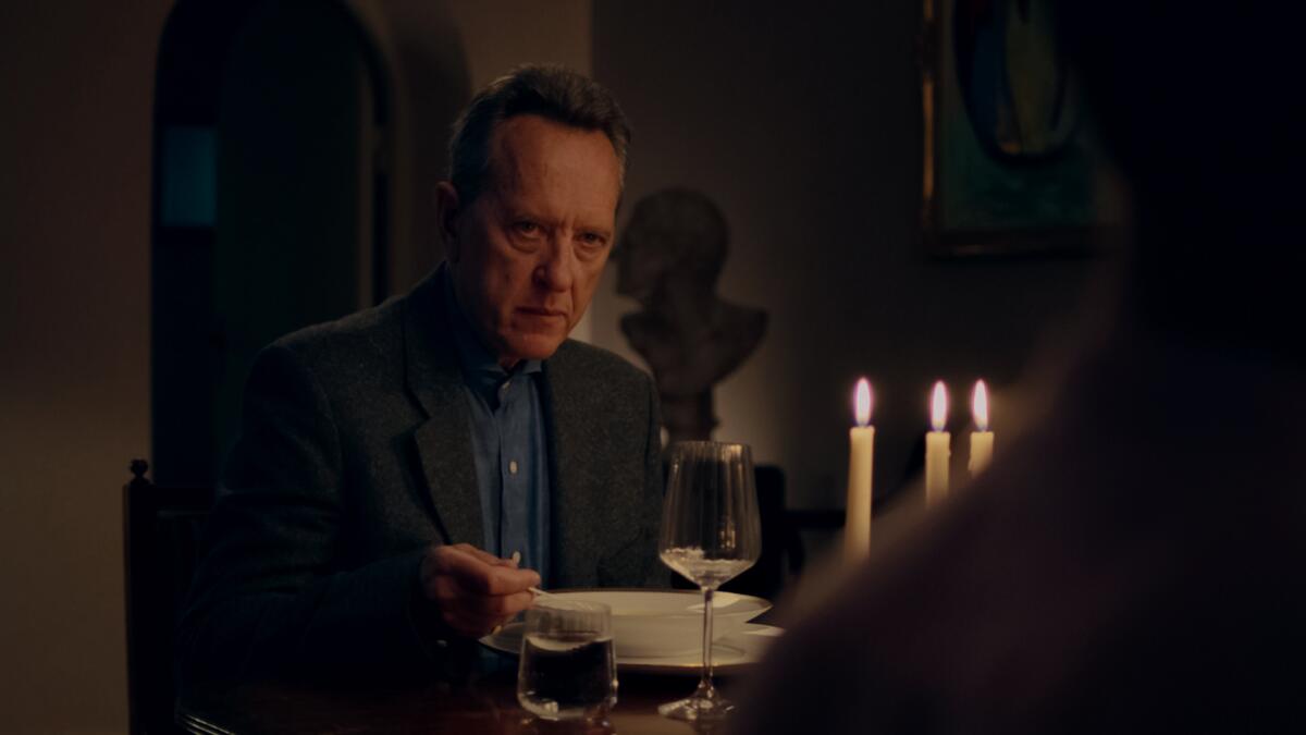 A man sits at a dining table by candlelight, eating soup.