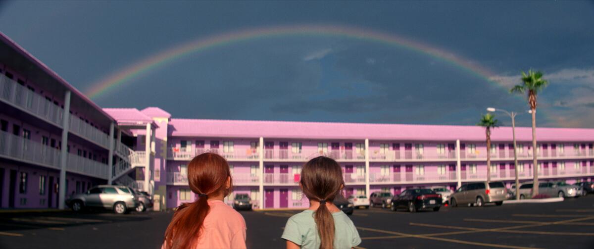 Two girls look at a rainbow over a pink motel.