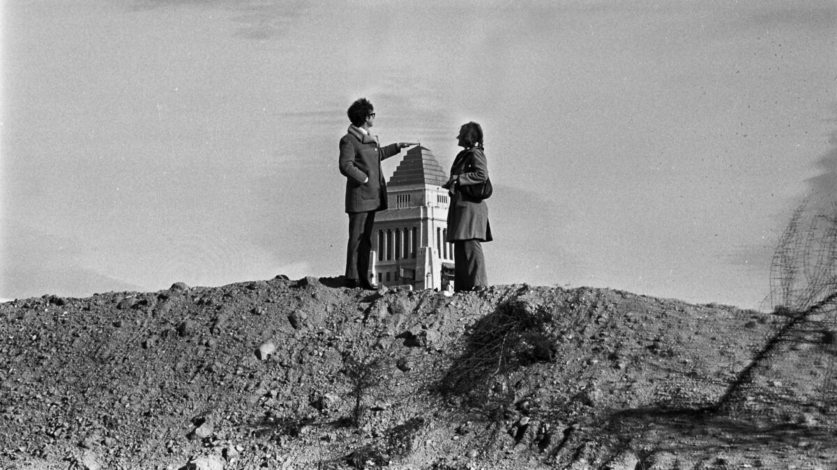 Hugh and Kim Grace stand atop a barren Bunker Hill in 1973 and pretend to touch the top of City Hall in the distance.