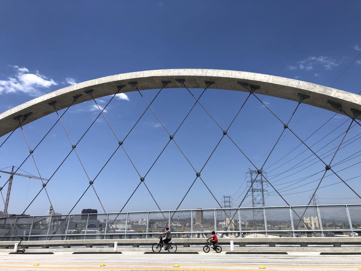 Two figures on bicycles are seen framed by one of the 6th Street Bridge's soaring arches