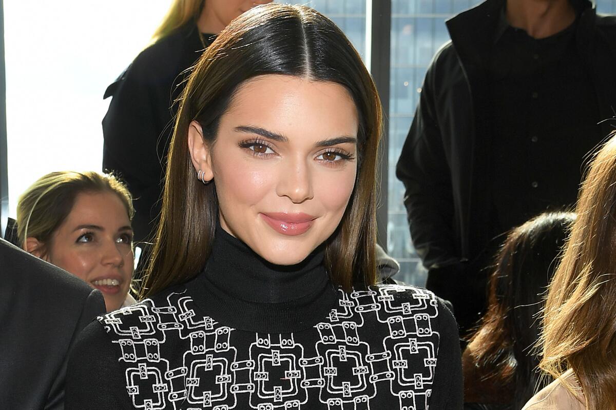 Kendall Jenner, wearing a striking turtleneck, stands amid a crowd.