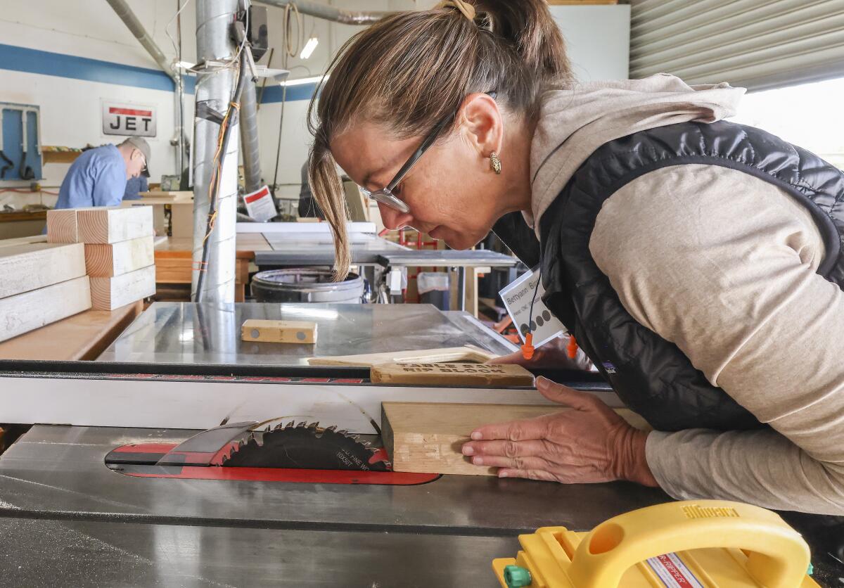 A woman aligns a block of wood over a saw in the San Diego Fine Woodworkers Association workshop.