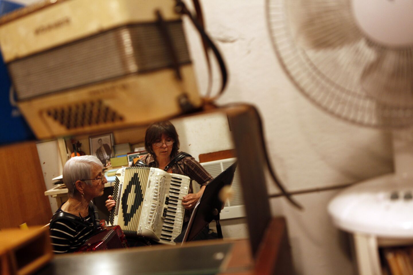 Veronika Caballero, right, wife of owner Dave Caballero, teaches Emily Gaughenbaugh, 92, how to play the accordion while caught in a reflection at Dave's Accordion School in Atwater Village. Gaughenbaugh said she took up the instrument a couple of months ago, in part because it beats doing crossword puzzles.