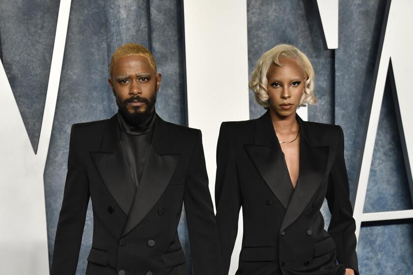 LaKeith Stanfield and Kasmere Trice posing in matching black suits on a blue carpet against a blue-and-white backdrop