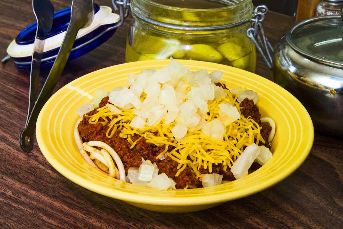 A bowl of noodles topped with chili, cheese and onion