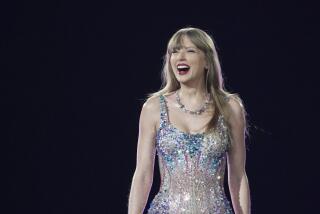 Taylor Swift in a bejeweled body suit and a necklace smiling and standing on a dark stage
