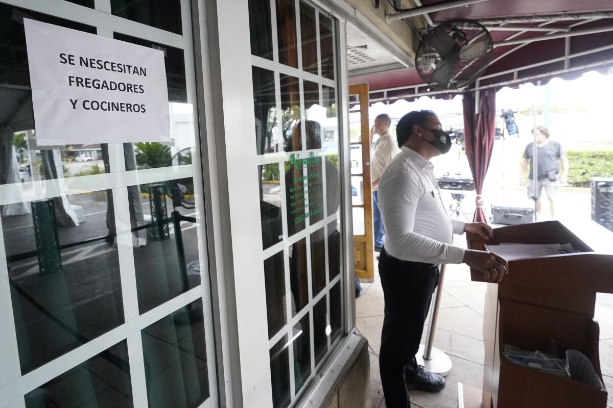 A host stands near a sign written in Spanish looking for dishwashers and cooks, Wednesday, July 14, 2021, in front of the Versailles Cuban restaurant in the Little Havana neighborhood of Miami. Growth in the services sector, where most Americans work, slowed in August after setting a record pace in July. The Institute for Supply Management reported Friday, Sept. 3 that its monthly survey of service industries decreased to a reading of 61.7 in August after hitting a record high of 64.1 in July. (AP Photo/Wilfredo Lee)