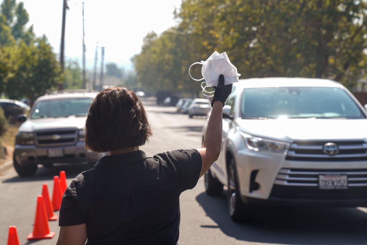 A woman wearing gloves holds up a stack of masks to hand out to drivers