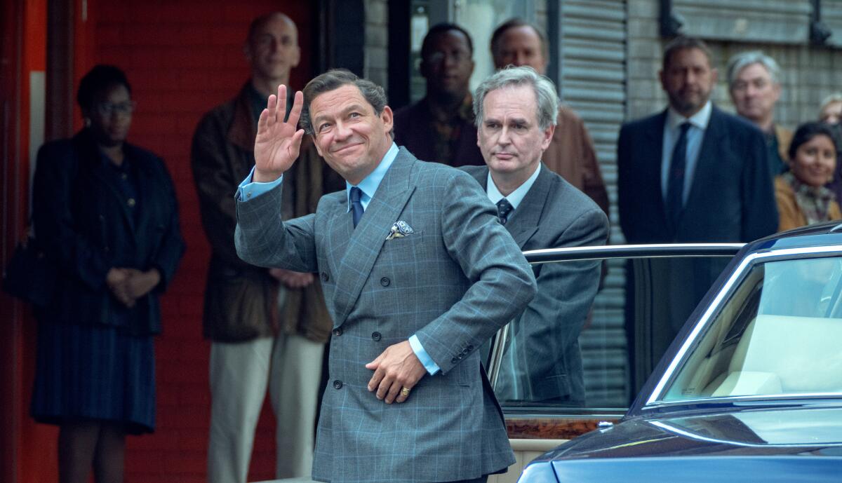 A man waves as he gets out of a car in "The Crown."