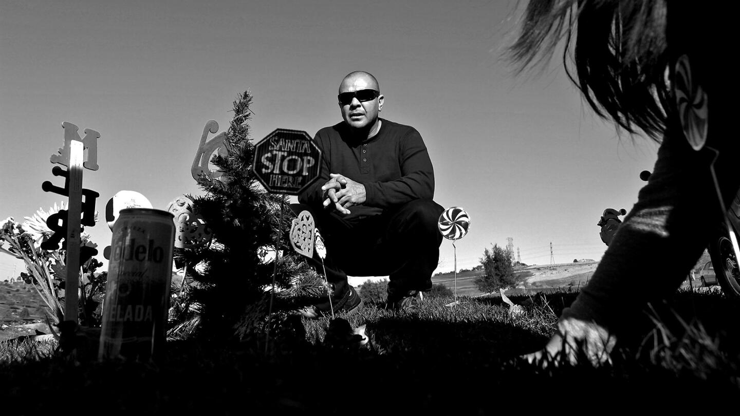 Rafael Madrigal kneels at his father's grave with daughter Kimberly, 12, after Christmas 2013 at Rose Hills Memorial Park in Whittier. Madrigal's father died while he was in prison.