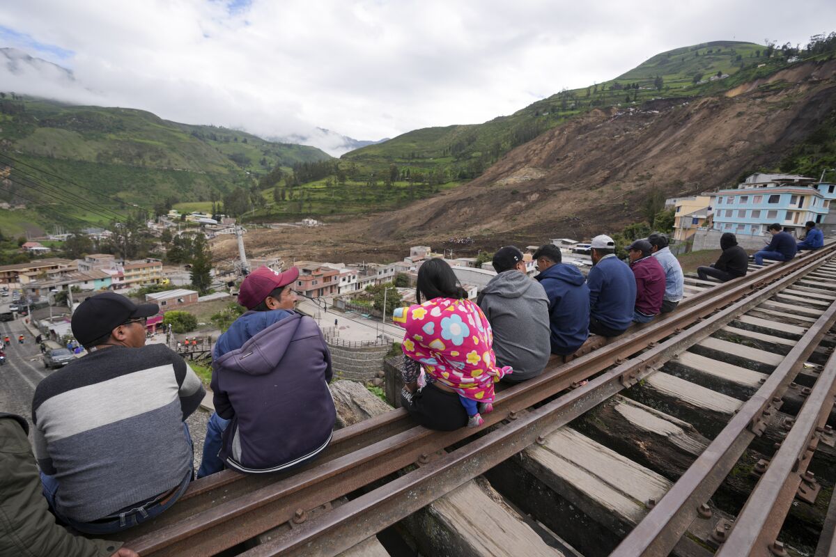 Residents sit on rail tracks overlooking a landslide in Alausi, Ecuador