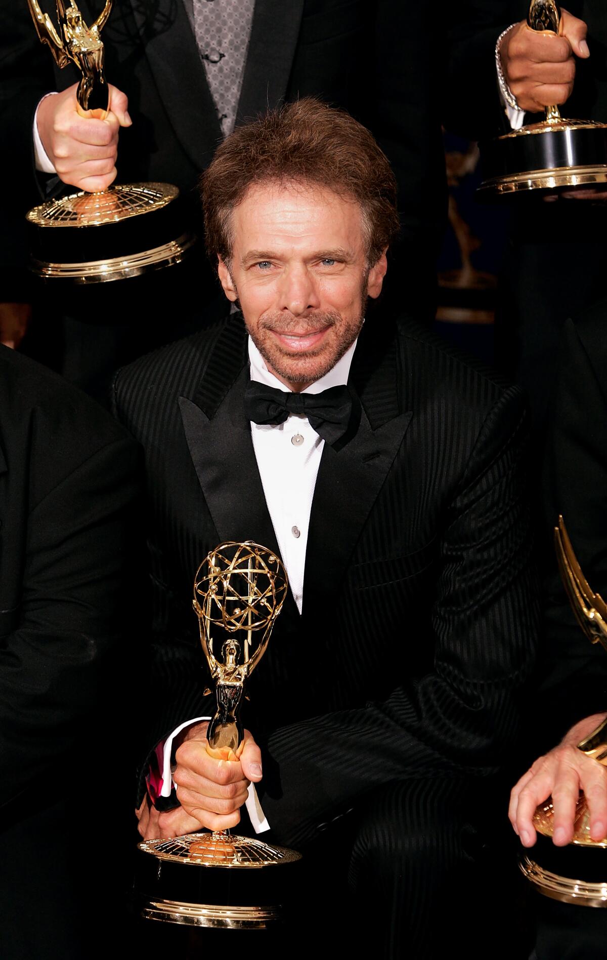 A man in a tuxedo holds an Emmy Award.