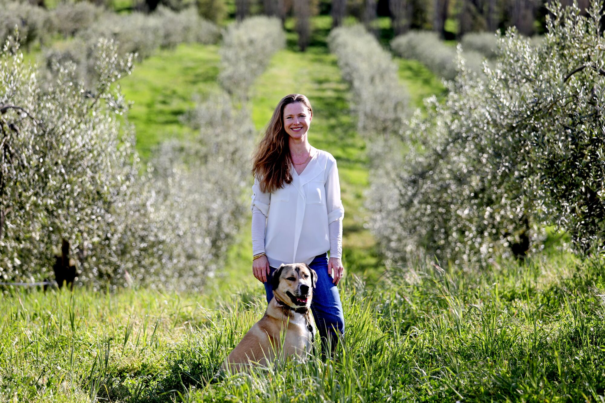 Samantha Dorsey stands with a dog in an olive grove.