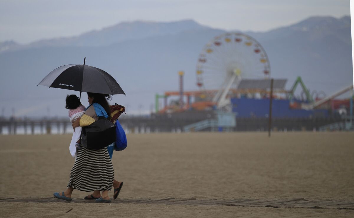 Umbrella-toting beachgoers walk across the beach amid rain showers in Santa Monica.