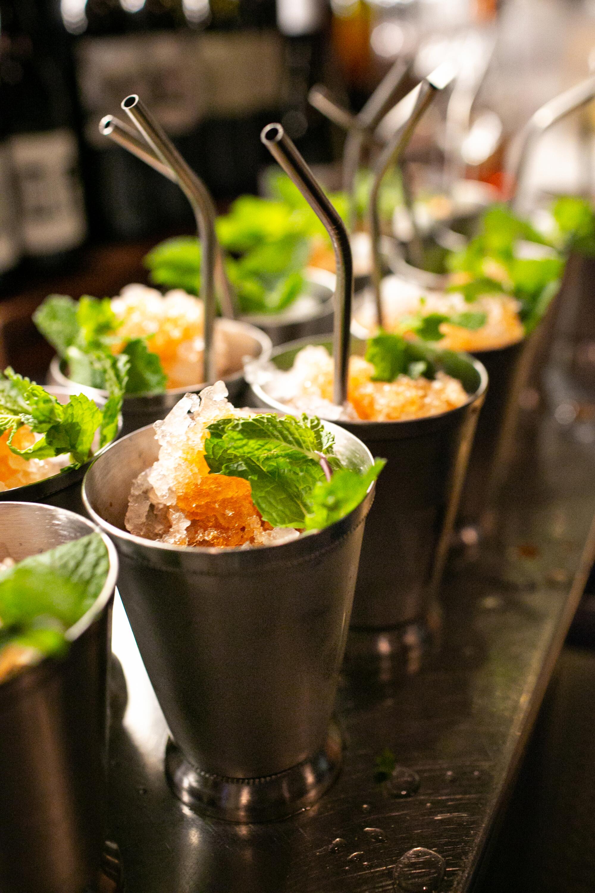 A double row of mint juleps in metal cups with metal straws.