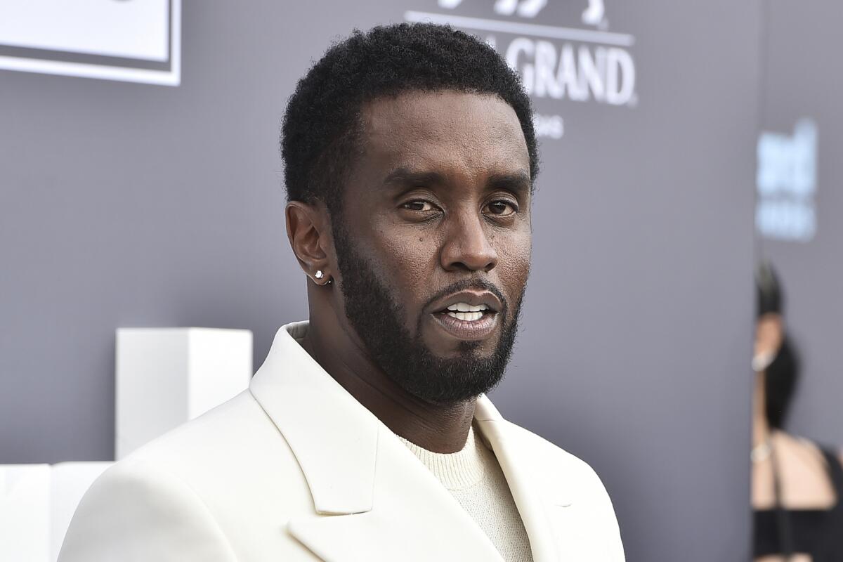 Sean 'Diddy' Combs in a white shirt and suit jacket posing against a gray background with white text