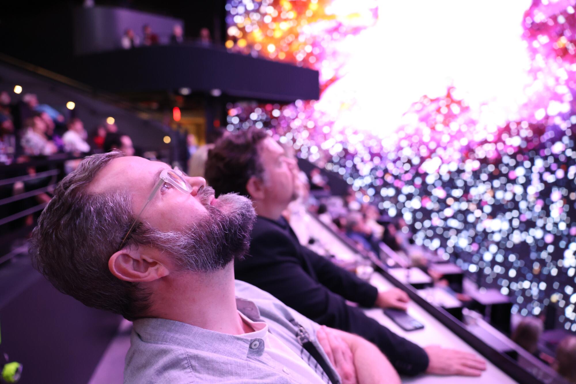 Audience members look up at an intergalactic scene on a screen. 