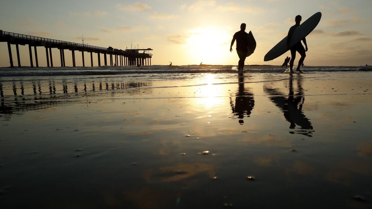 Surfers leave the water next to Scripps Pier, where researchers this month logged the highest sea surface temperatures ever recorded in 102 years of taking measurements at the La Jolla pier.