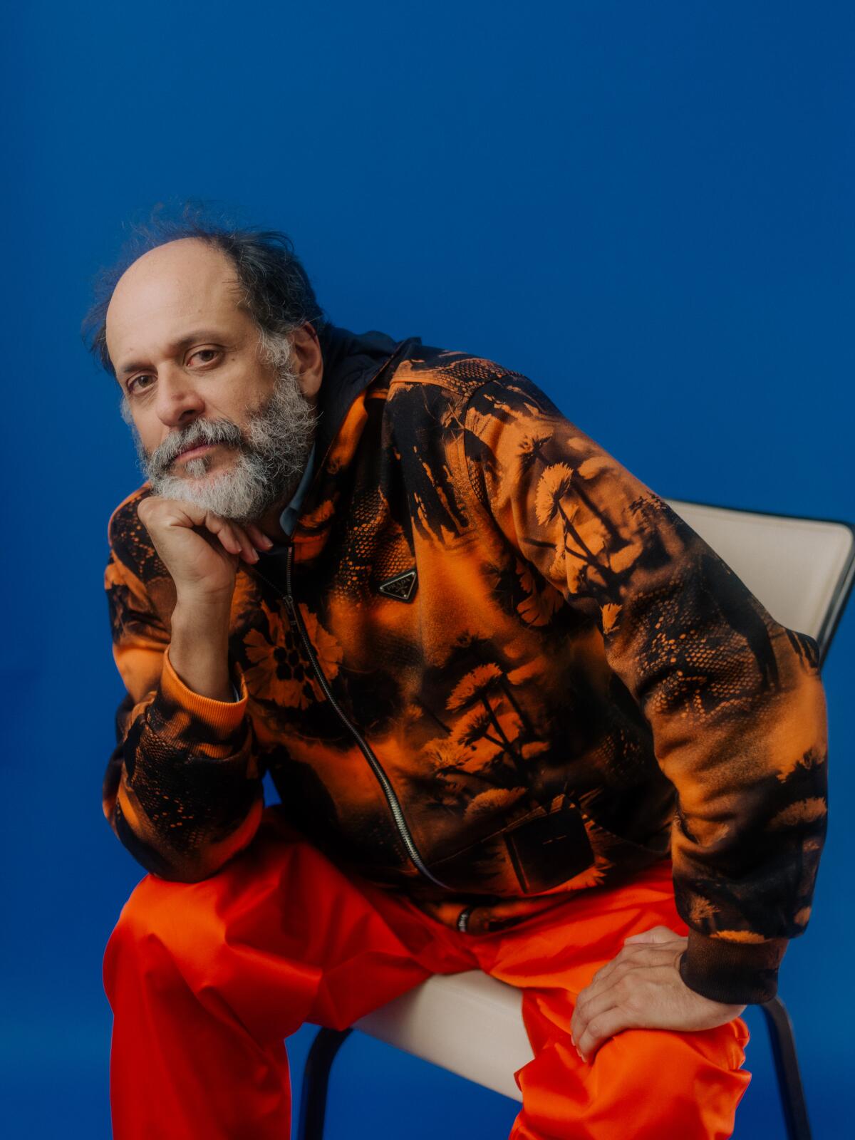 Luca Guadagnino wears bright clothing and rests his elbow on his knee and his chin on his hand for a portrait.